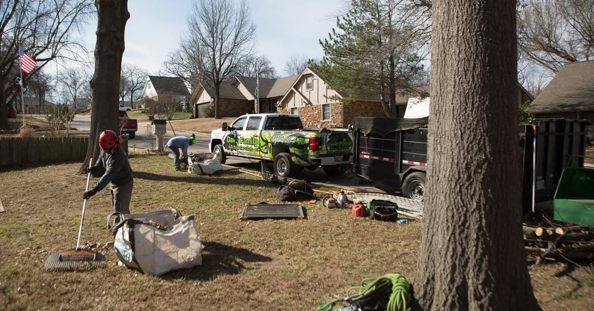 Two helmeted crew members raking debris in a front yard beside the Davis Family Arbor truck