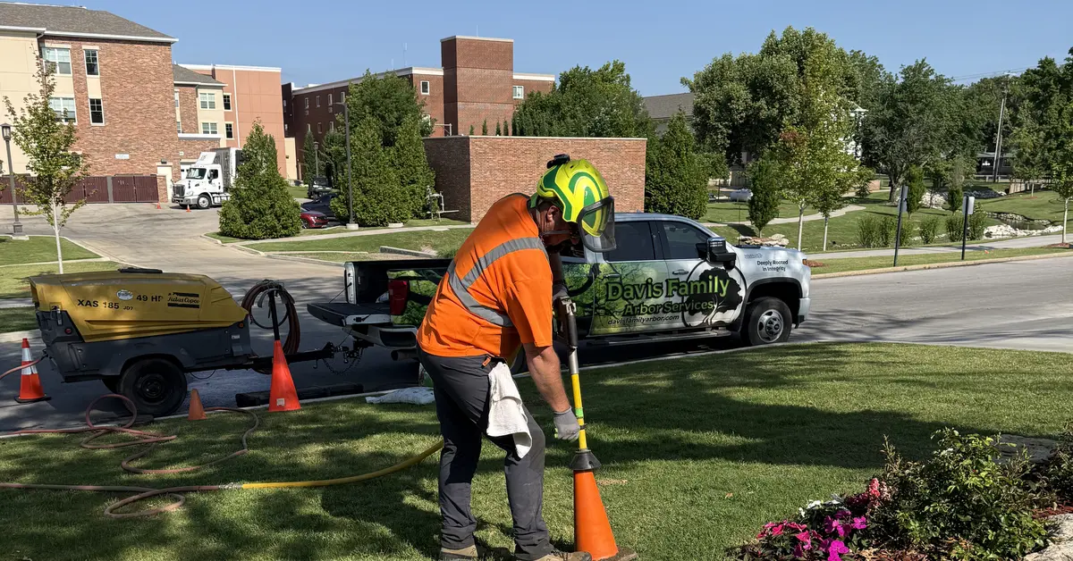 Davis Family Arbor technician using an AirSpade and air compressor to excavate soil in a landscape bed